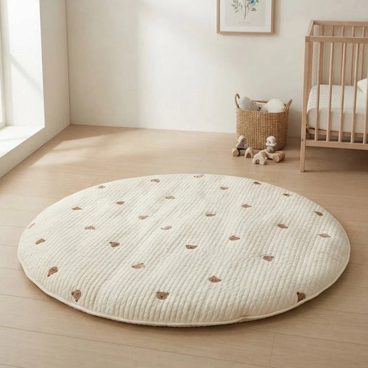 Tapis d'éveil rond matelassé crème brodé de petits oursons, posé au sol dans une chambre d'enfant